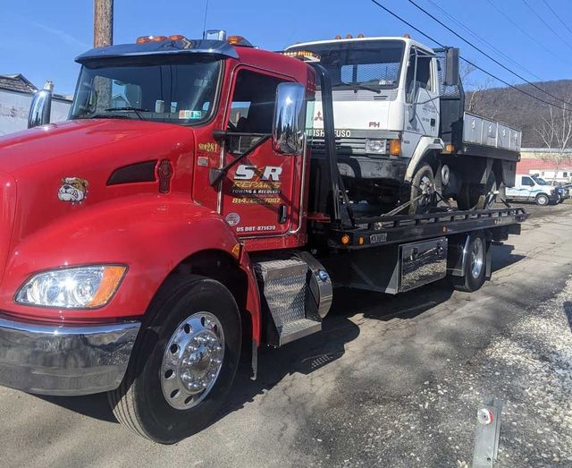 Red tow truck carrying a white dump truck on a flatbed in a snowy lot