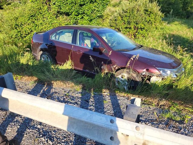 Maroon sedan crashed off the road in a grassy ditch beside a guardrail.