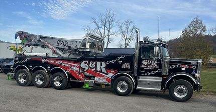 Black tow truck with red and white graphics parked outdoors under a blue sky