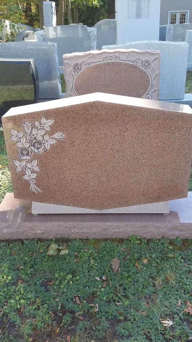 Two granite gravestones in a cemetery, the front one pink with a curved top and white floral etching.