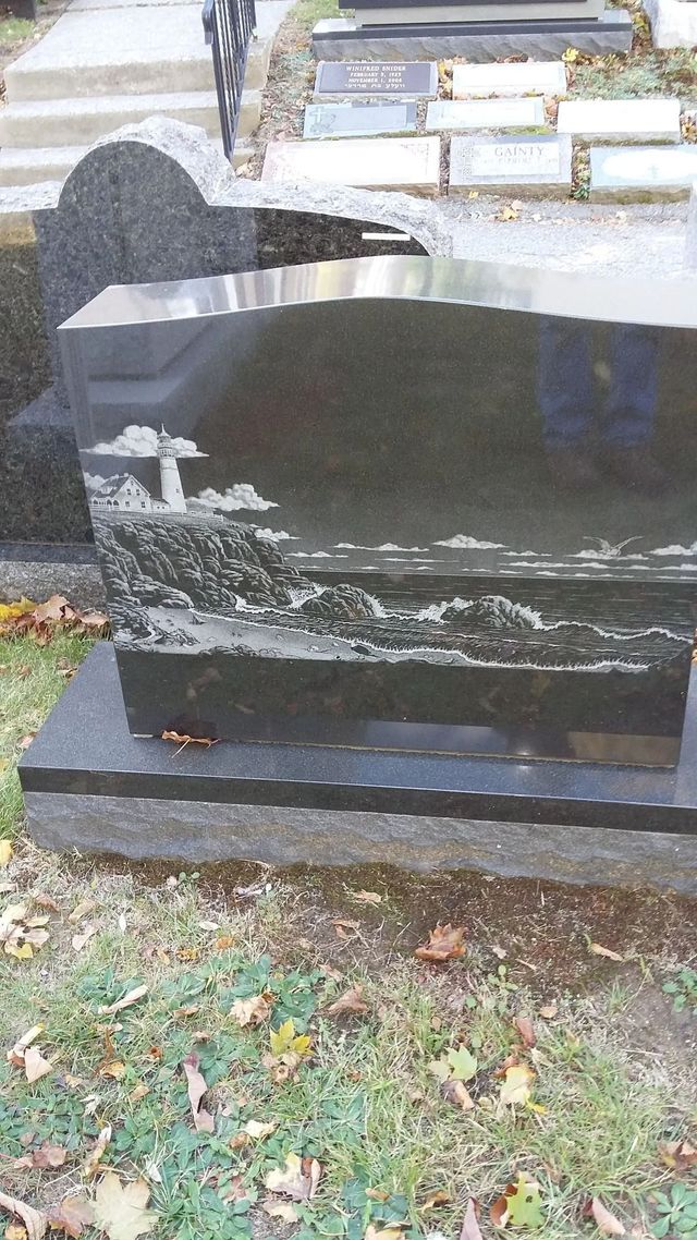 Black polished gravestone with a white landscape engraving in a grassy cemetery.