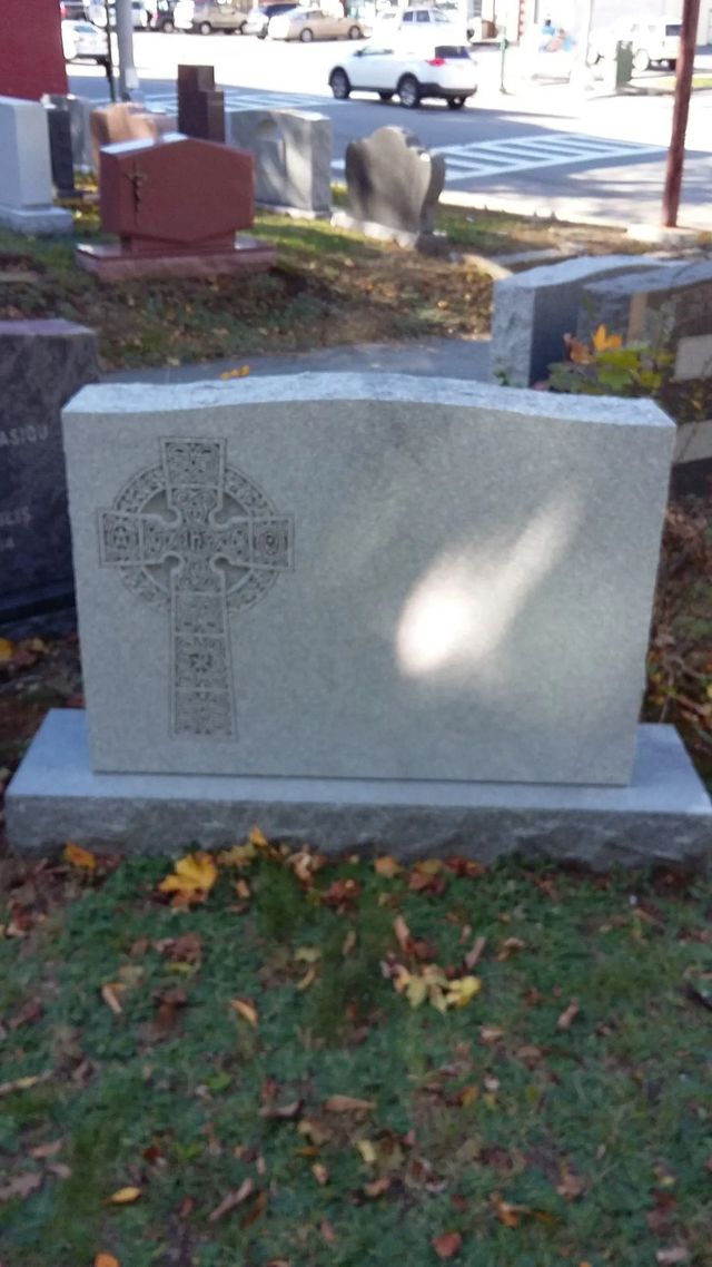 Gray gravestone with a carved cross in a grassy cemetery