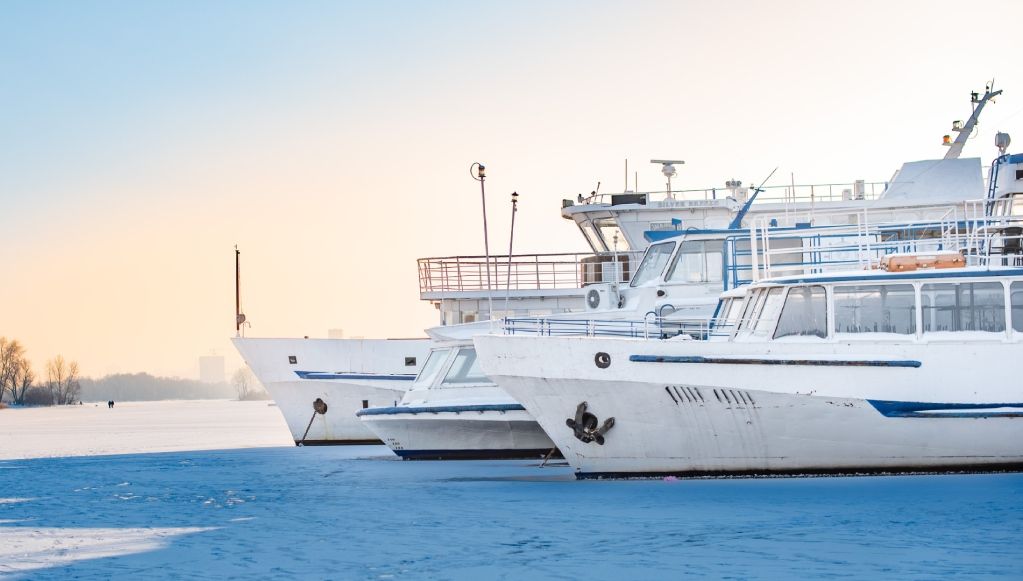Learn More About Marine Insurance A close-up view of three large white passenger boats docked in a row, surrounded by thick blue ice and snow
