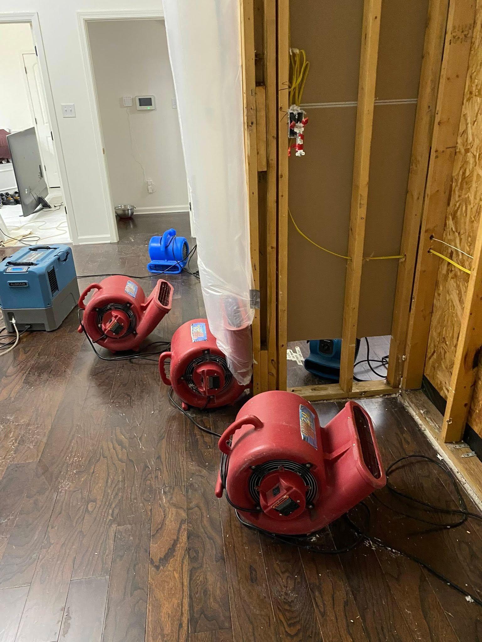 Industrial fans and dehumidifiers placed in a room undergoing water damage restoration, with exposed wall studs.