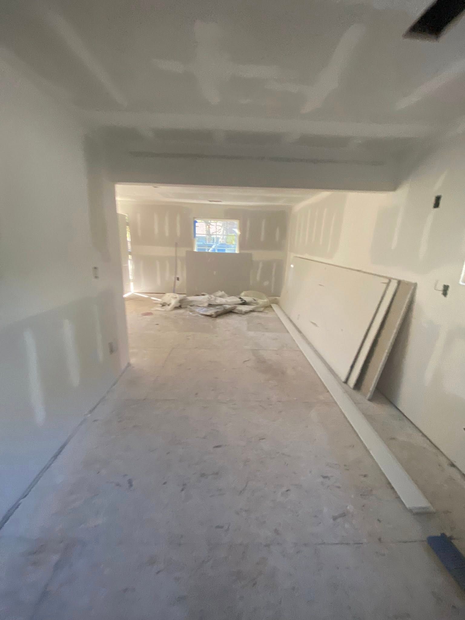 An unfinished room with newly hung drywall, a concrete floor, and stacks of drywall panels leaning against the wall.