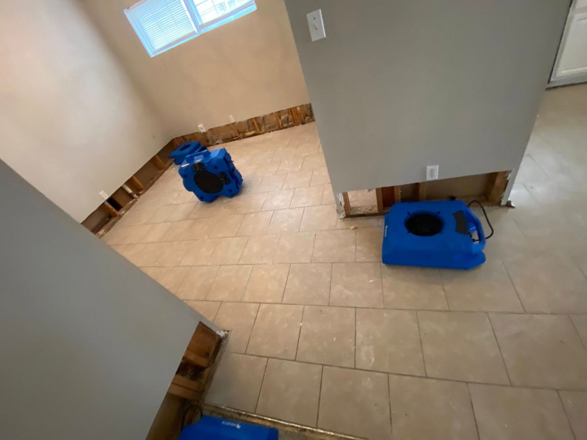 Water damage restoration in a room with tiled floors, exposed wall studs, and blue air movers set up for drying.