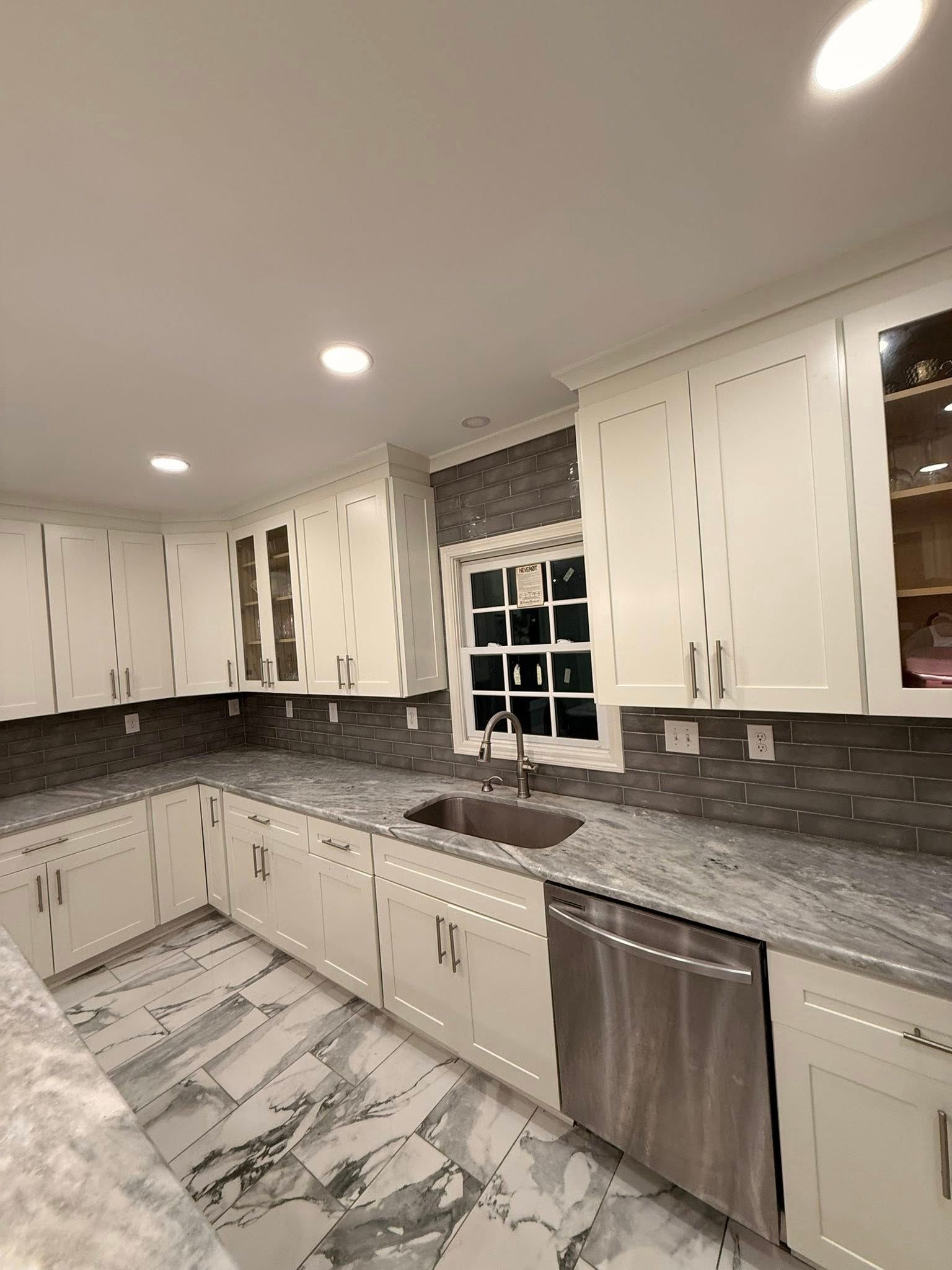 A modern kitchen featuring white cabinets, grey granite countertops, a dark grey subway tile backsplash, and marble floors.