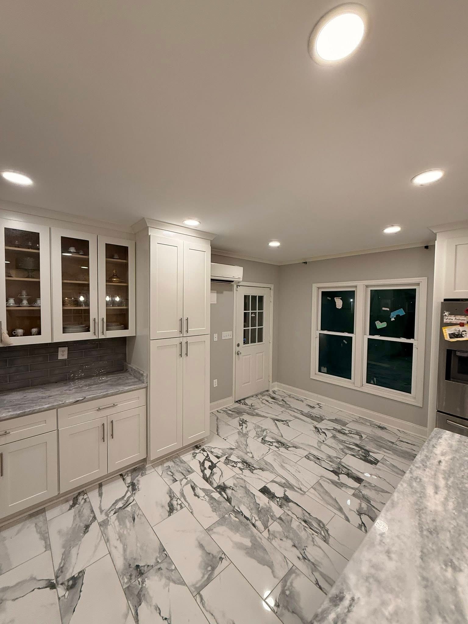 A kitchen with white cabinets, dark marble countertops, matching marble-patterned tile floors, and a glass-paneled door.