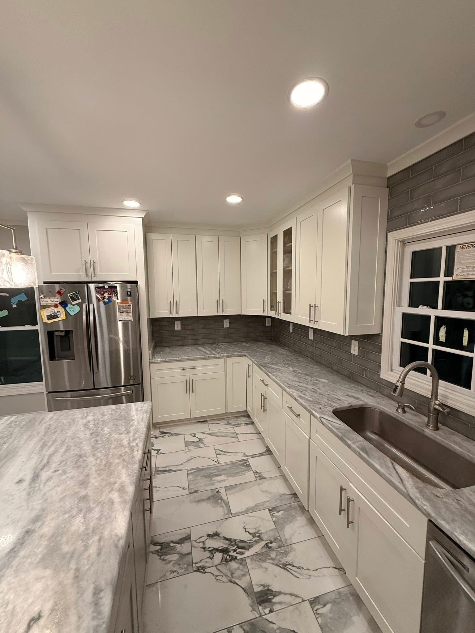 A modern kitchen featuring white cabinets, grey marble-style countertops, stainless steel appliances, and tiled flooring.