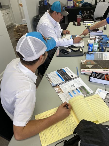Workers in high-visibility vests renovate the exterior of a two-story brick house with plywood covering a front window.
