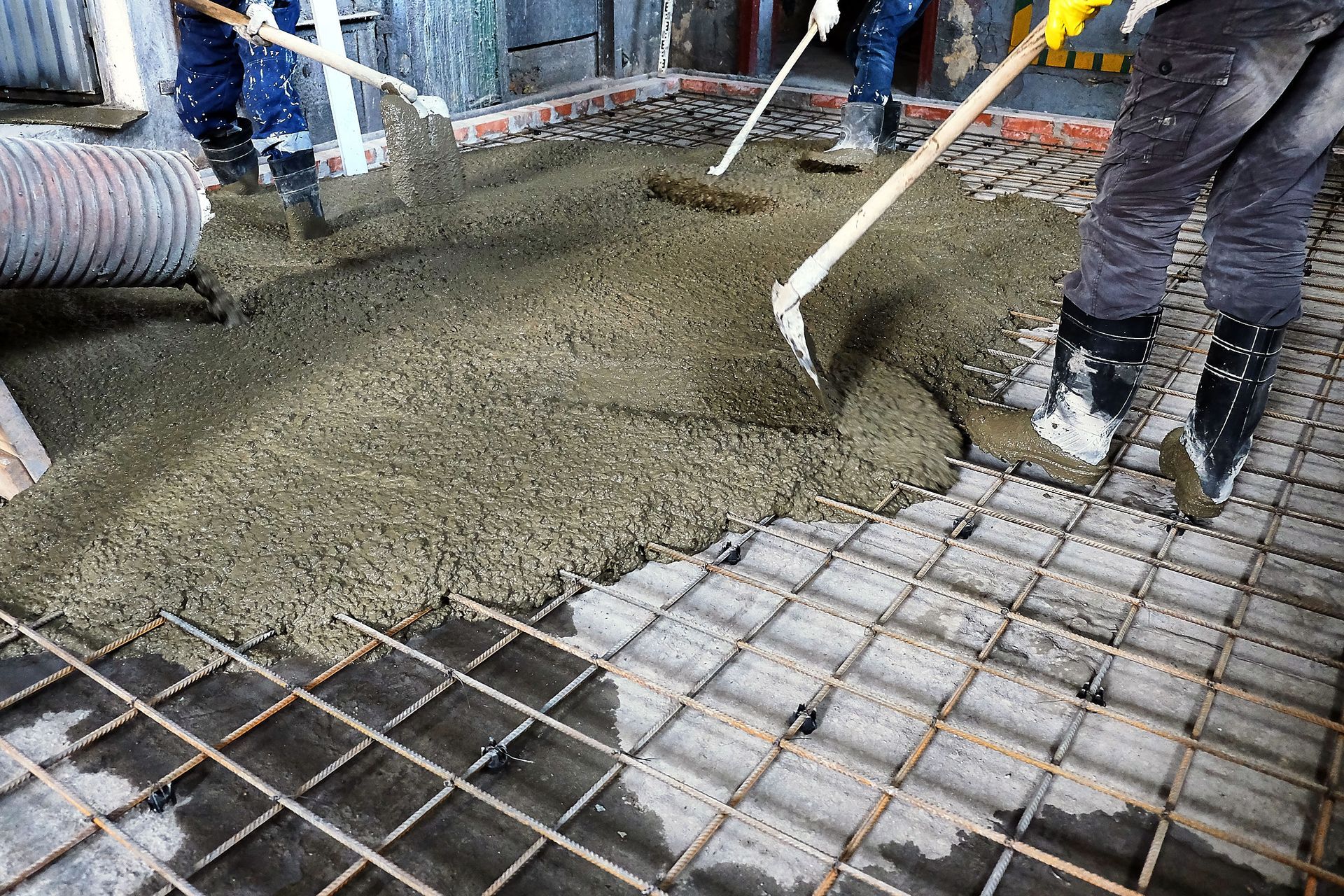 Construction workers pouring concrete over metal rebar on a building floor.