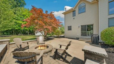 Patio with fire pit and wooden chairs in front of a two-story house and colorful tree.