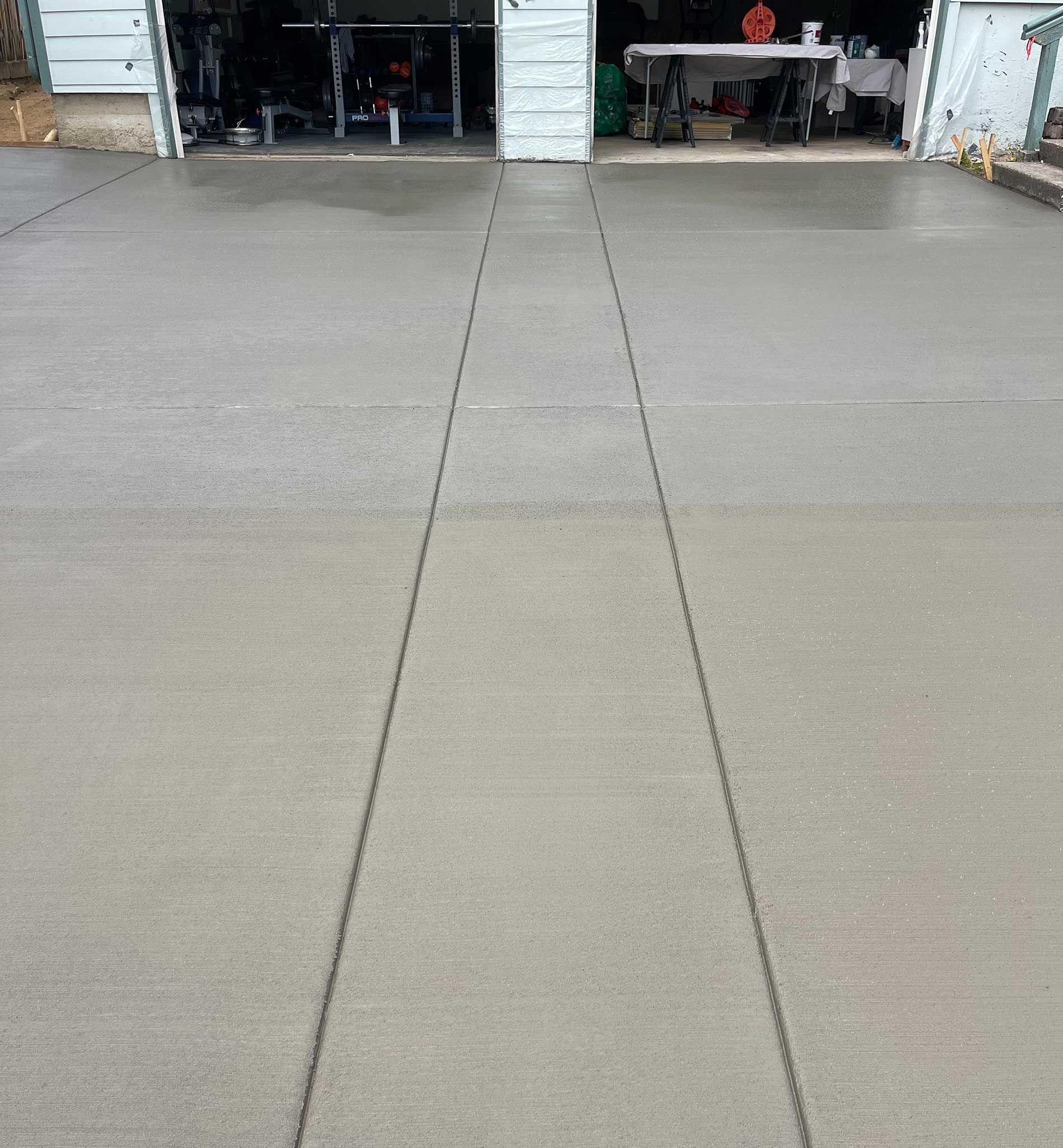 Freshly poured concrete driveway with two control joints leading to a garage.