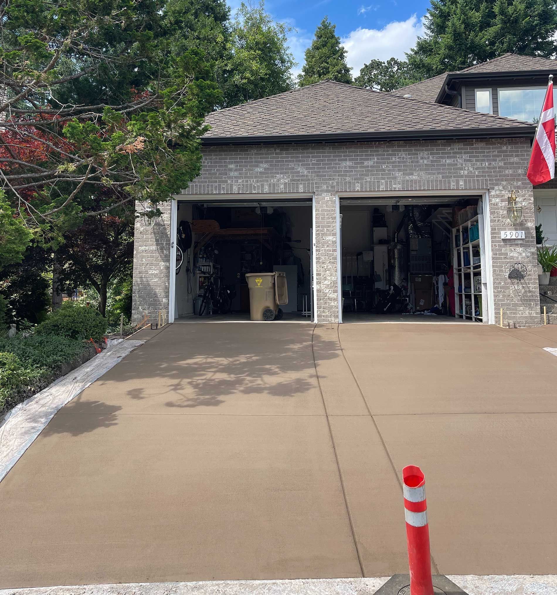 Garage with two open doors, a concrete driveway, and a red and white traffic marker.