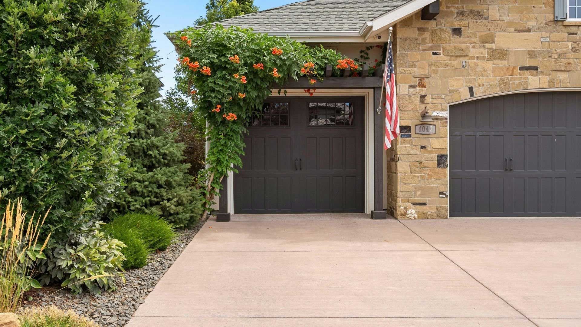 Garage with gray doors, flowering vines, flag, and driveway.