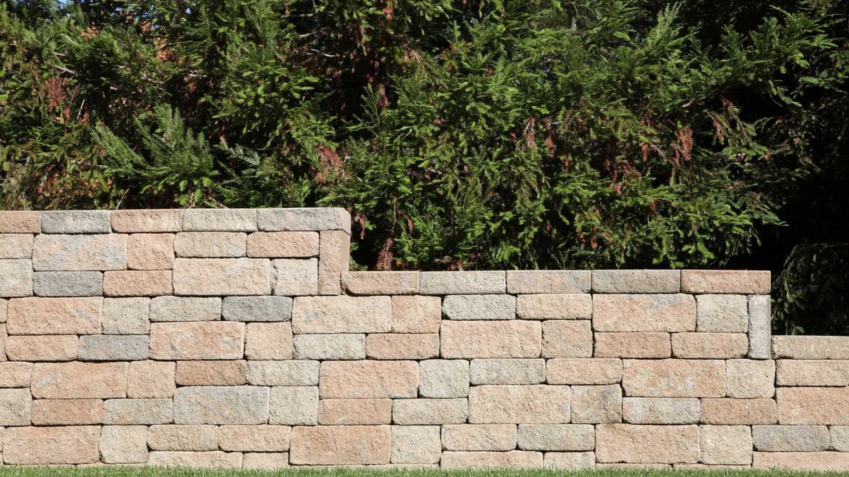 Stone retaining wall with green bushes behind it.