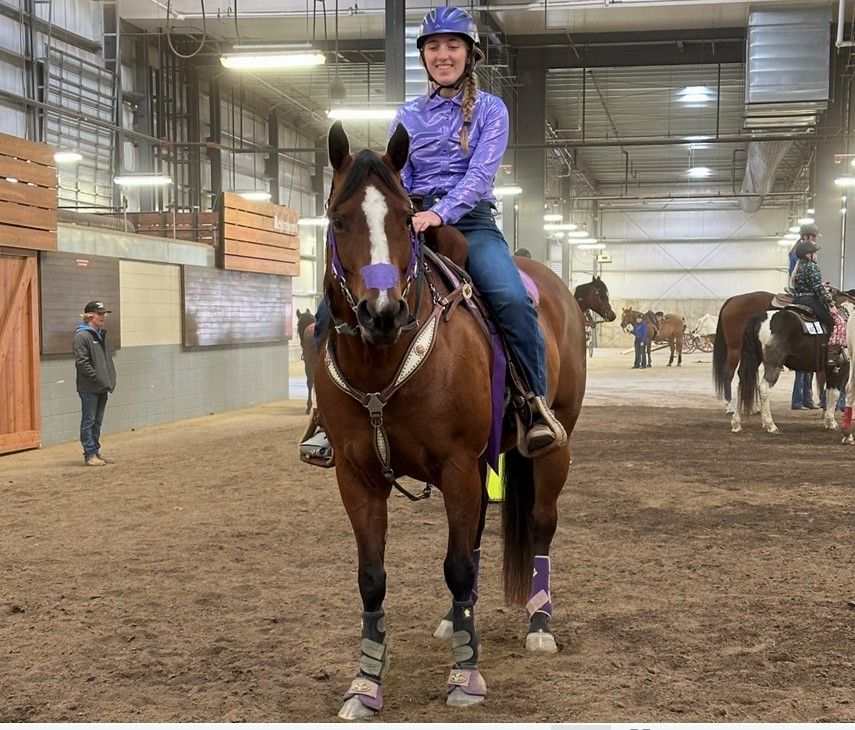 A woman is riding a brown horse in an indoor arena.