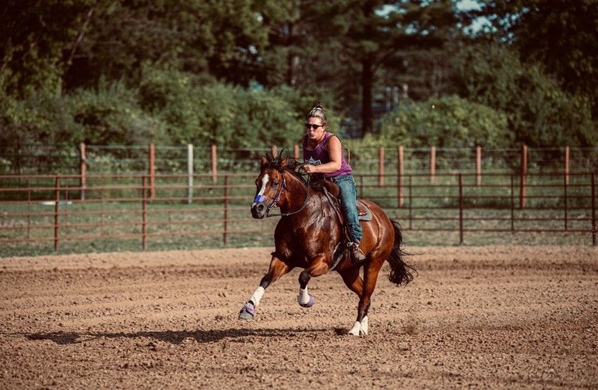 A woman is riding a brown horse in a dirt field.