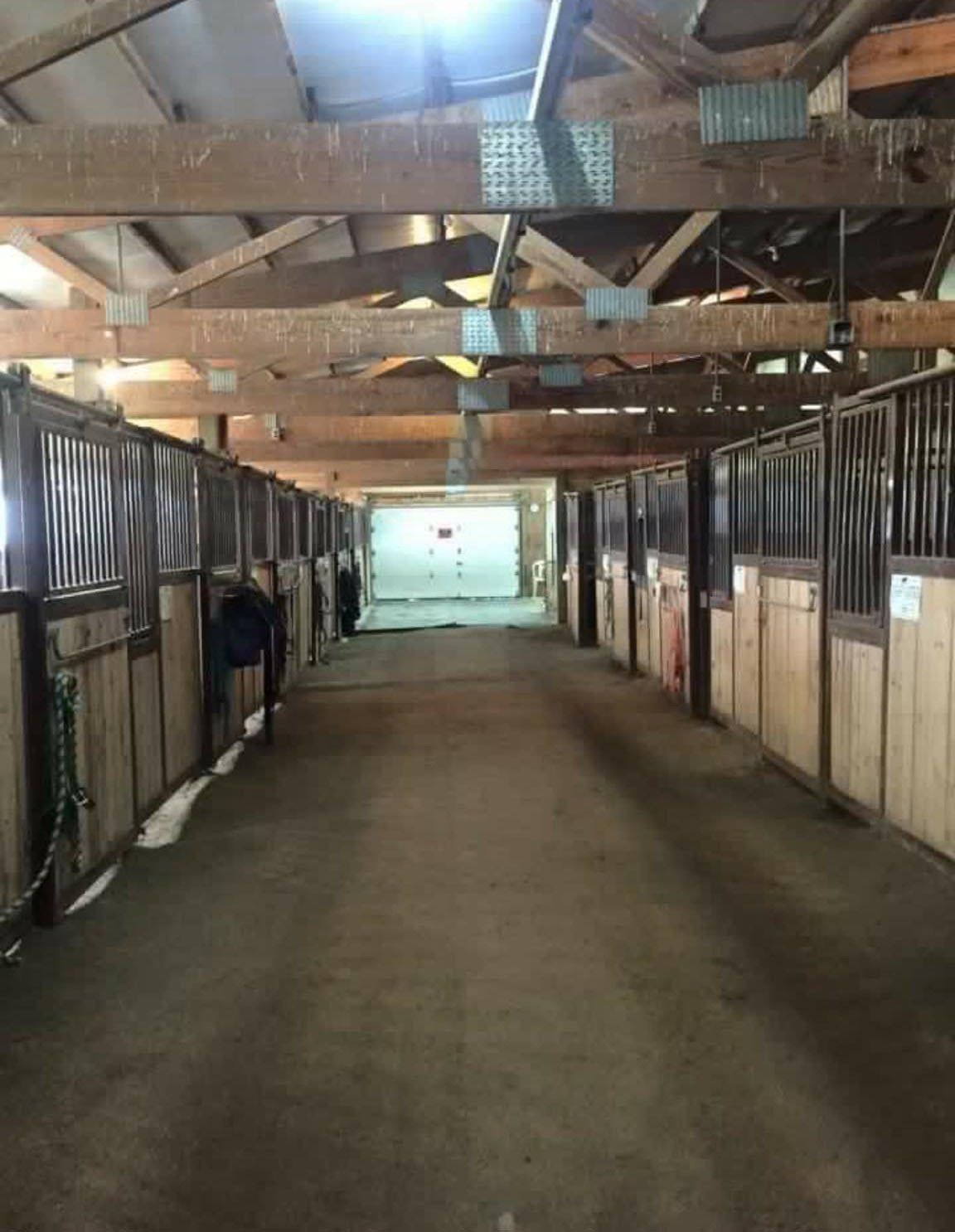A long hallway in a horse stable with lots of boxes