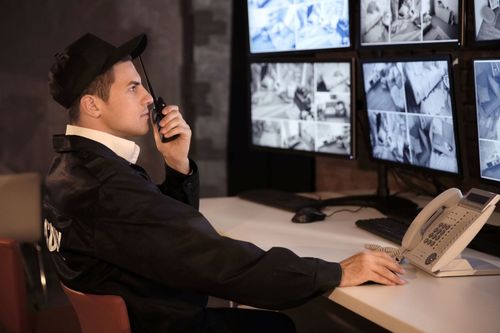 Security guard monitoring multiple surveillance screens while speaking into a walkie-talkie at a desk