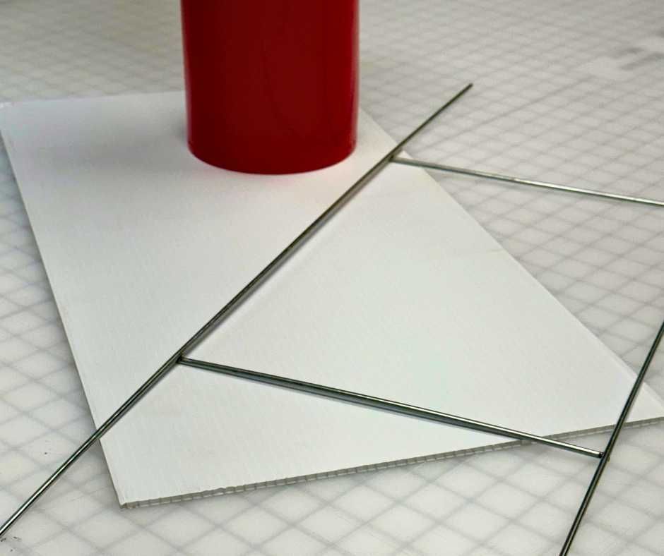 A white corrugated plastic sign blank sits on a grid mat next to a red cylindrical object and a wire yard sign stake