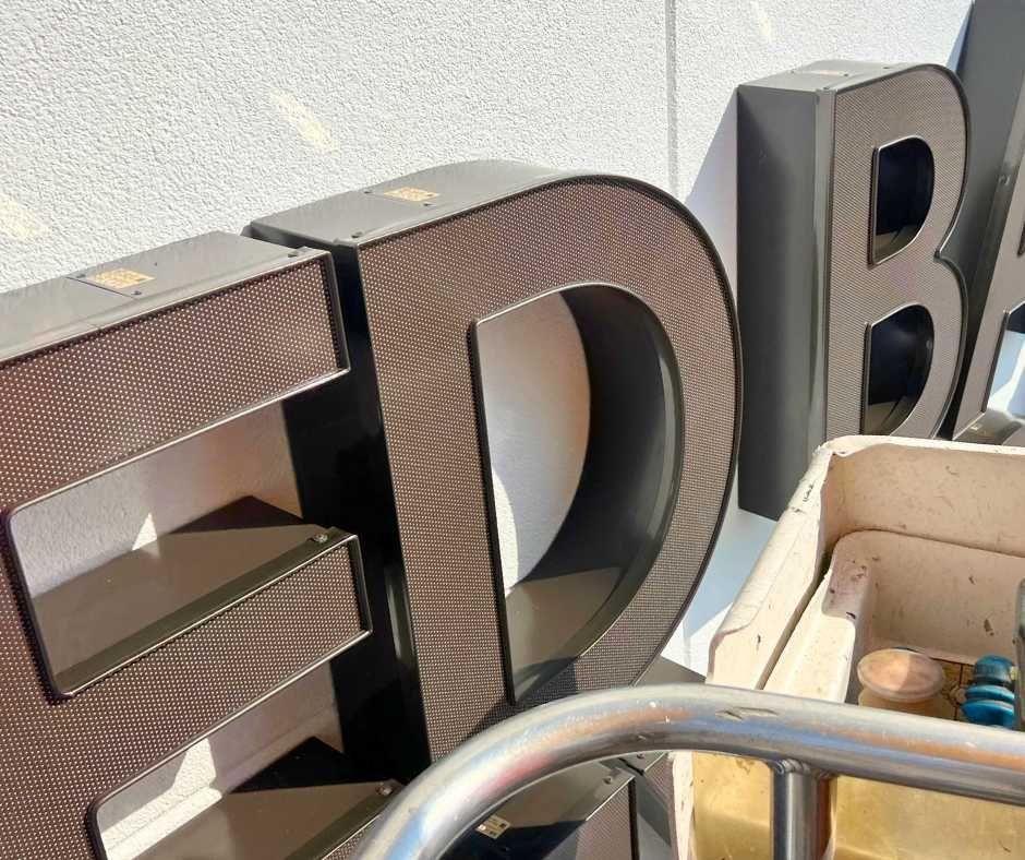 Large, three-dimensional, textured brown letters standing outdoors, partially overlapping