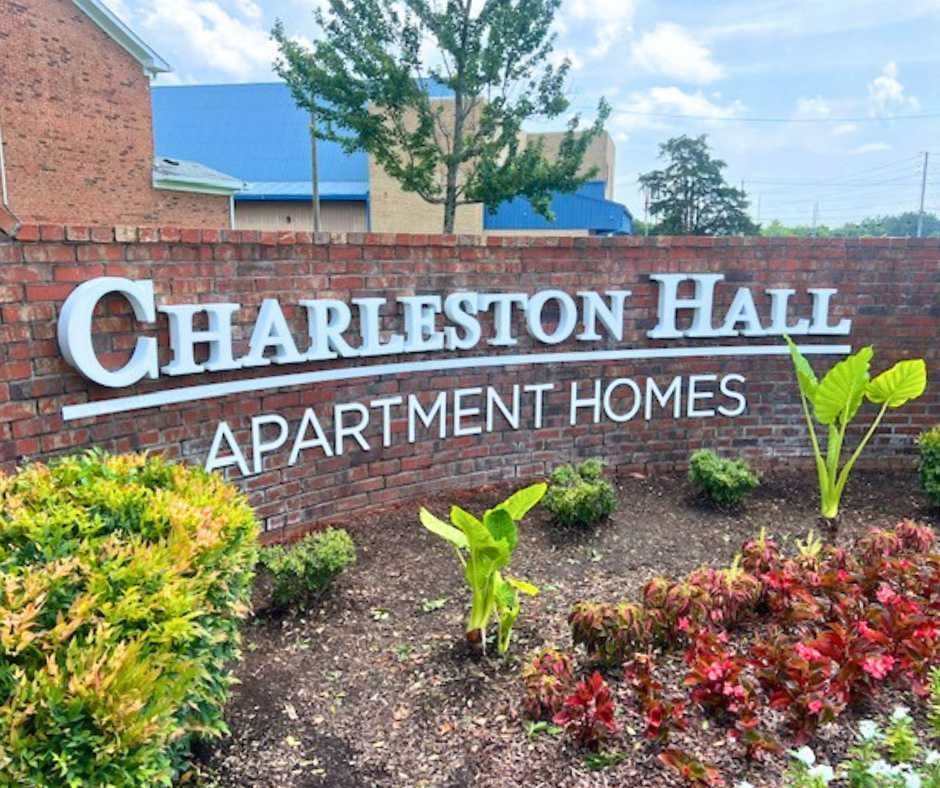 A brick wall with white lettering that reads Charleston Hall Apartment Homes, surrounded by green and red landscaping