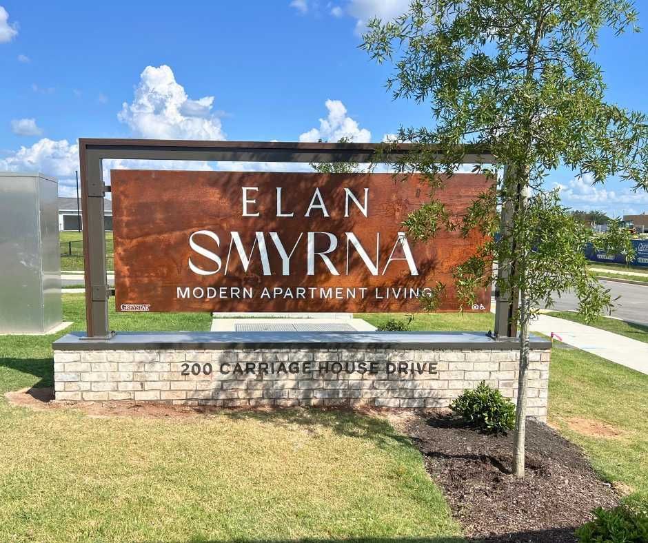 A sign for Elan Smyrna modern apartment living located at 200 Carriage House Drive, set on a brick base outdoors