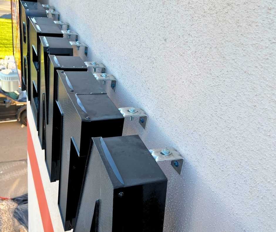 A row of black, three-dimensional channel letters mounted to a light-colored building exterior using metal brackets