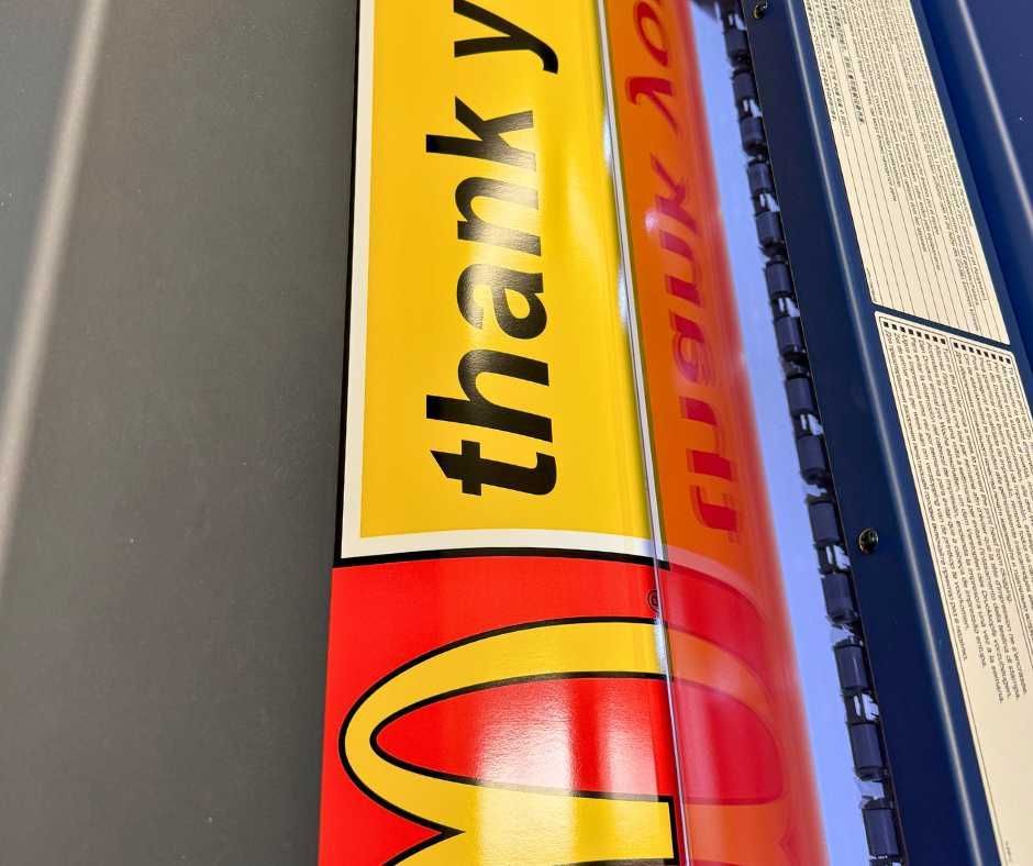 A McDonald’s sign being fed through a printer, showing the thank you text and golden arches on red and yellow vinyl