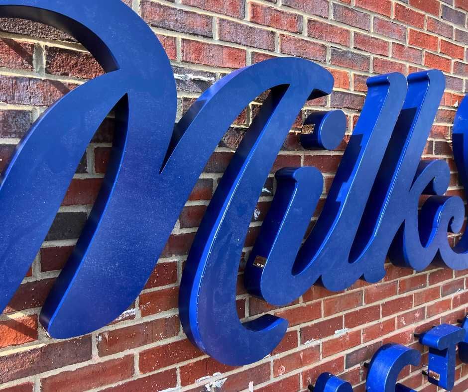 Blue, three-dimensional script lettering mounted on a reddish-brown brick wall