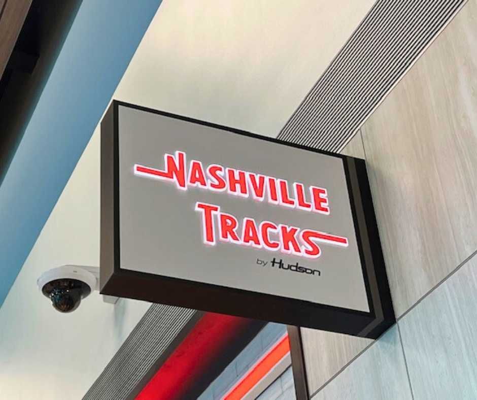 A rectangular, hanging sign for Nashville Tracks by Hudson, featuring red stylized text against a light gray background