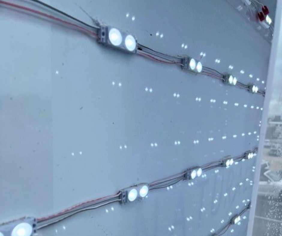 Rows of LED modules wired together and mounted on a white surface, illuminated and glowing brightly