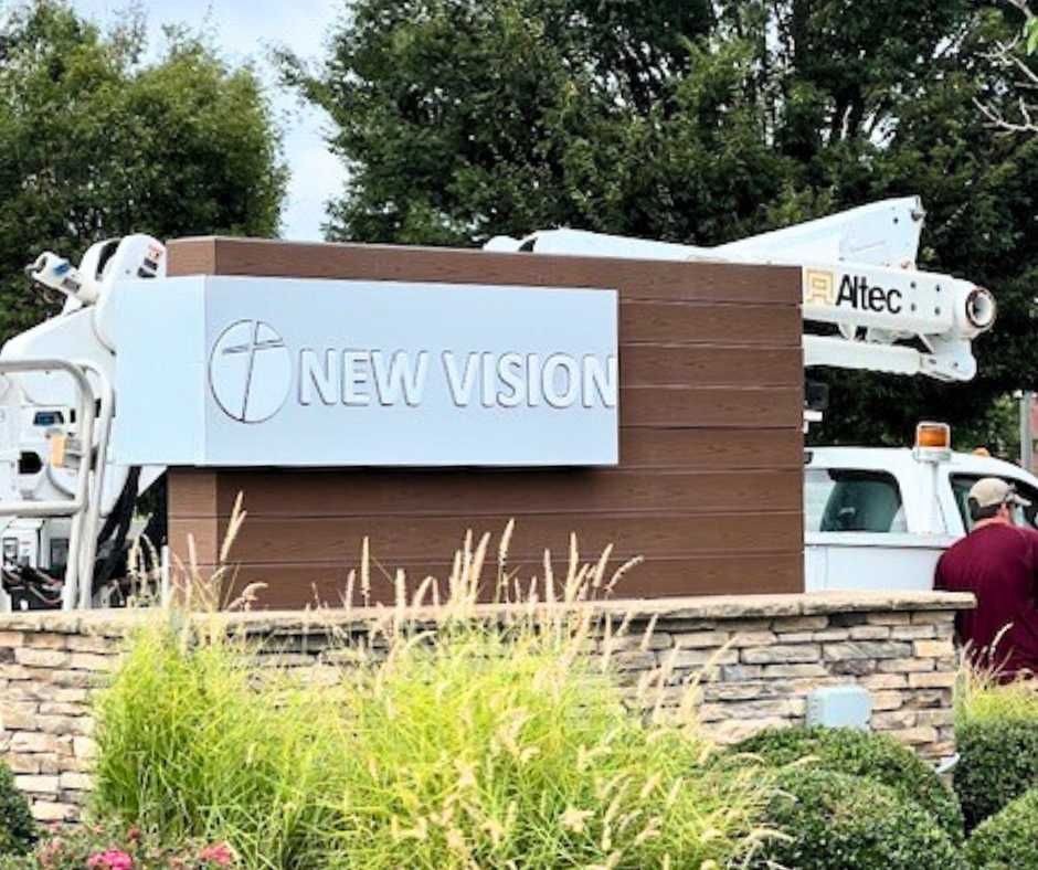 A New Vision sign mounted on a brick and wood pedestal, with a utility truck parked behind it