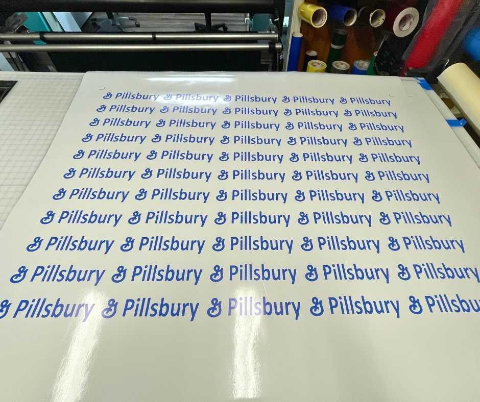 A large white sheet on a workstation table features repeated blue Pillsbury brand logos arranged in orderly rows