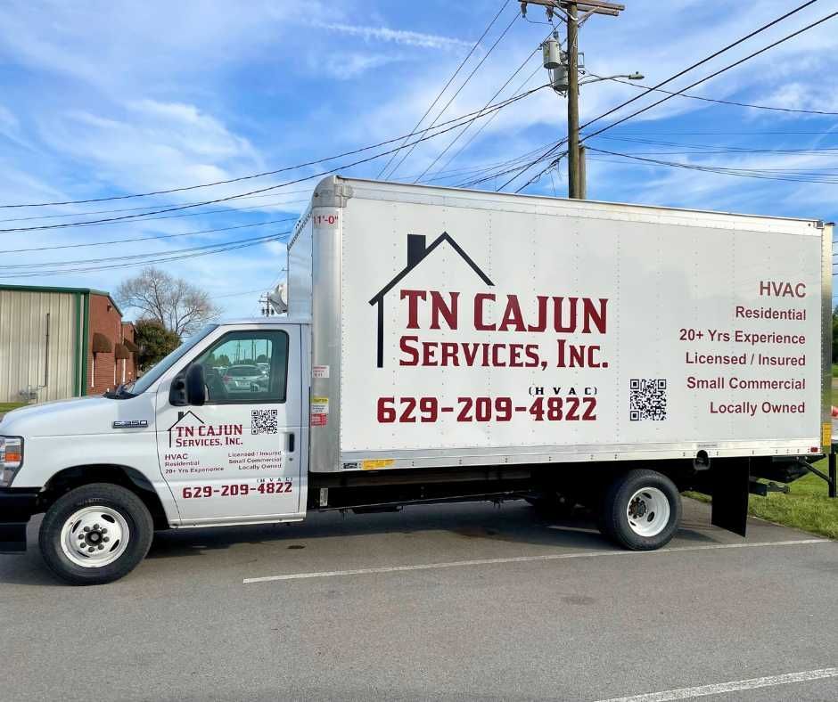 A white TN Cajun Services box truck parked on asphalt under a blue sky, displaying company contact information and logo