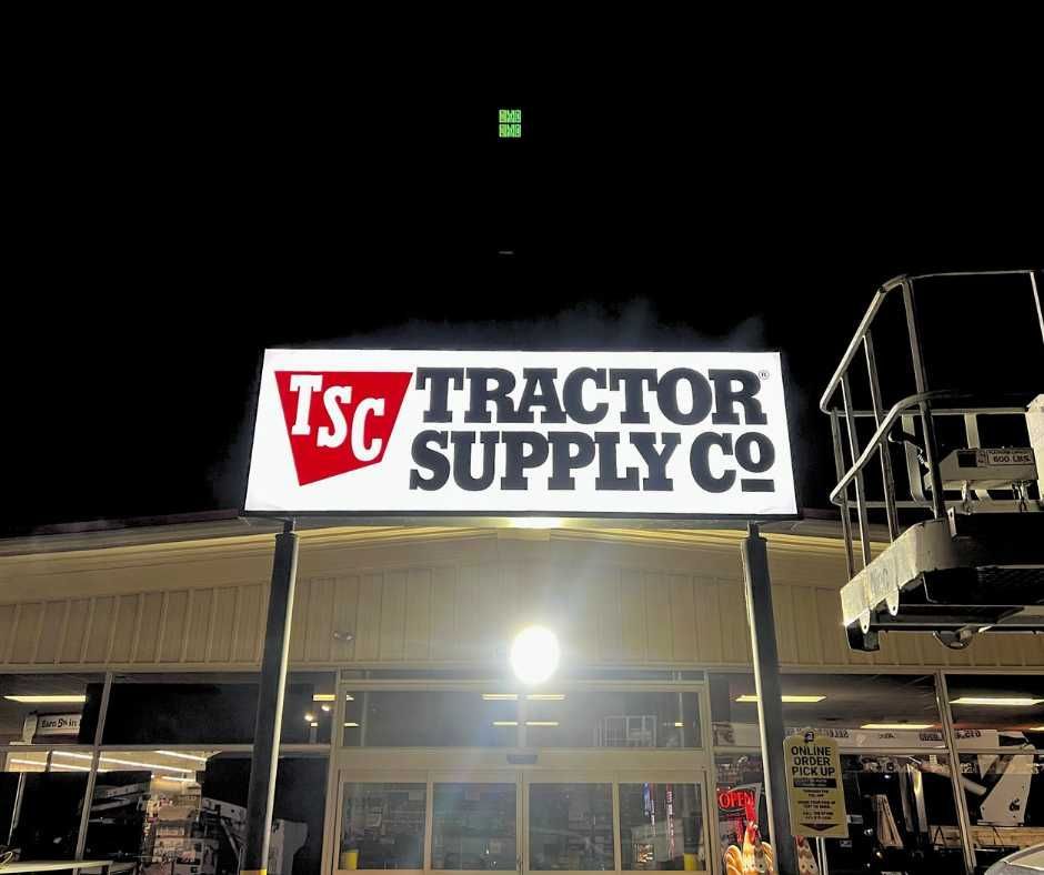 A glowing Tractor Supply Co. sign mounted on poles in front of a store entrance at night