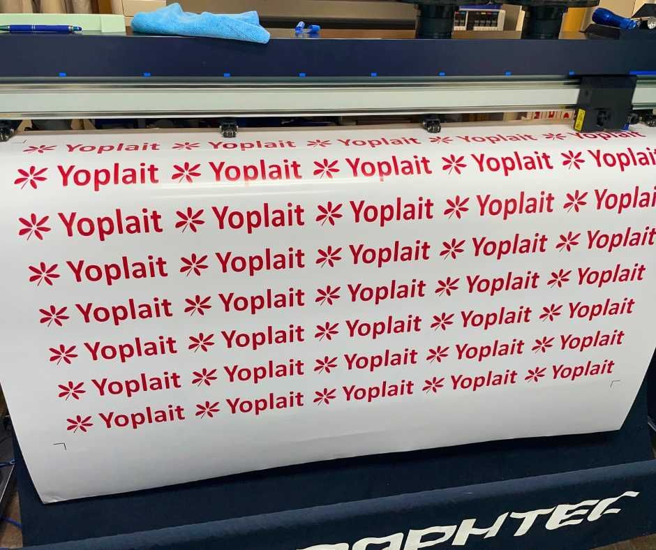 A large white sheet on a Graphtec cutting machine, printed with repeating red Yoplait brand logos