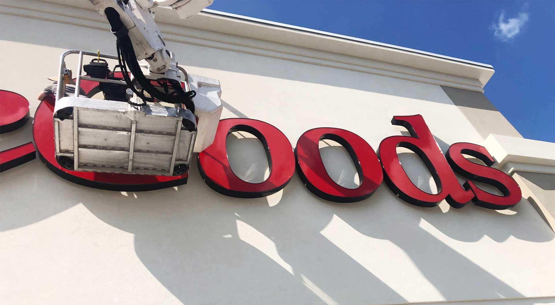 Bucket truck working on the red "Goods" sign of a TJ Maxx store under a blue sky.