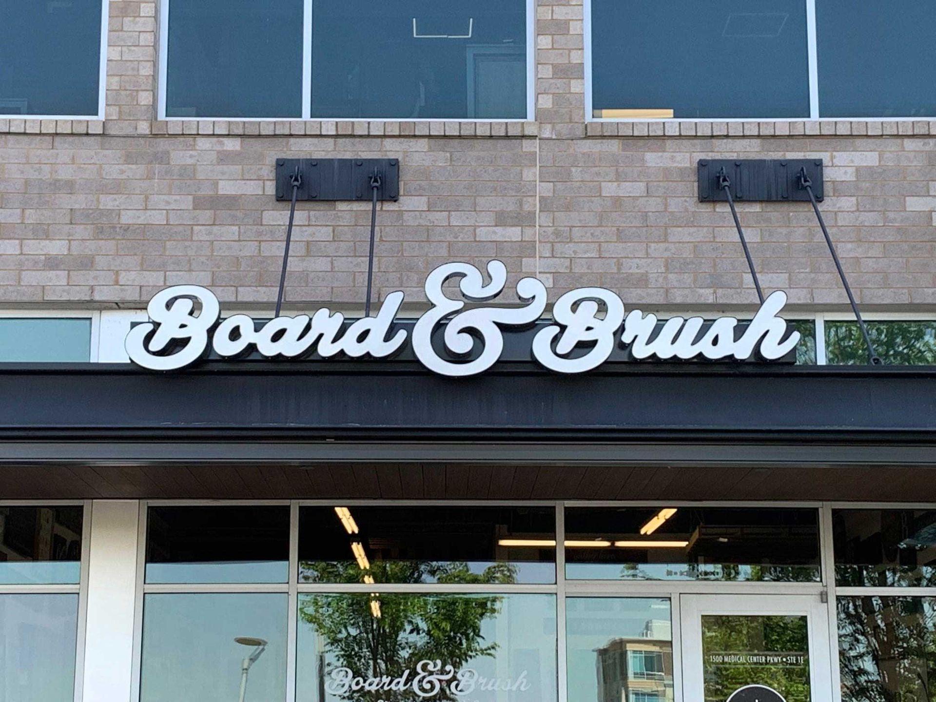 Board & Brush sign on a brick building with large windows. White lettering on a black awning.
