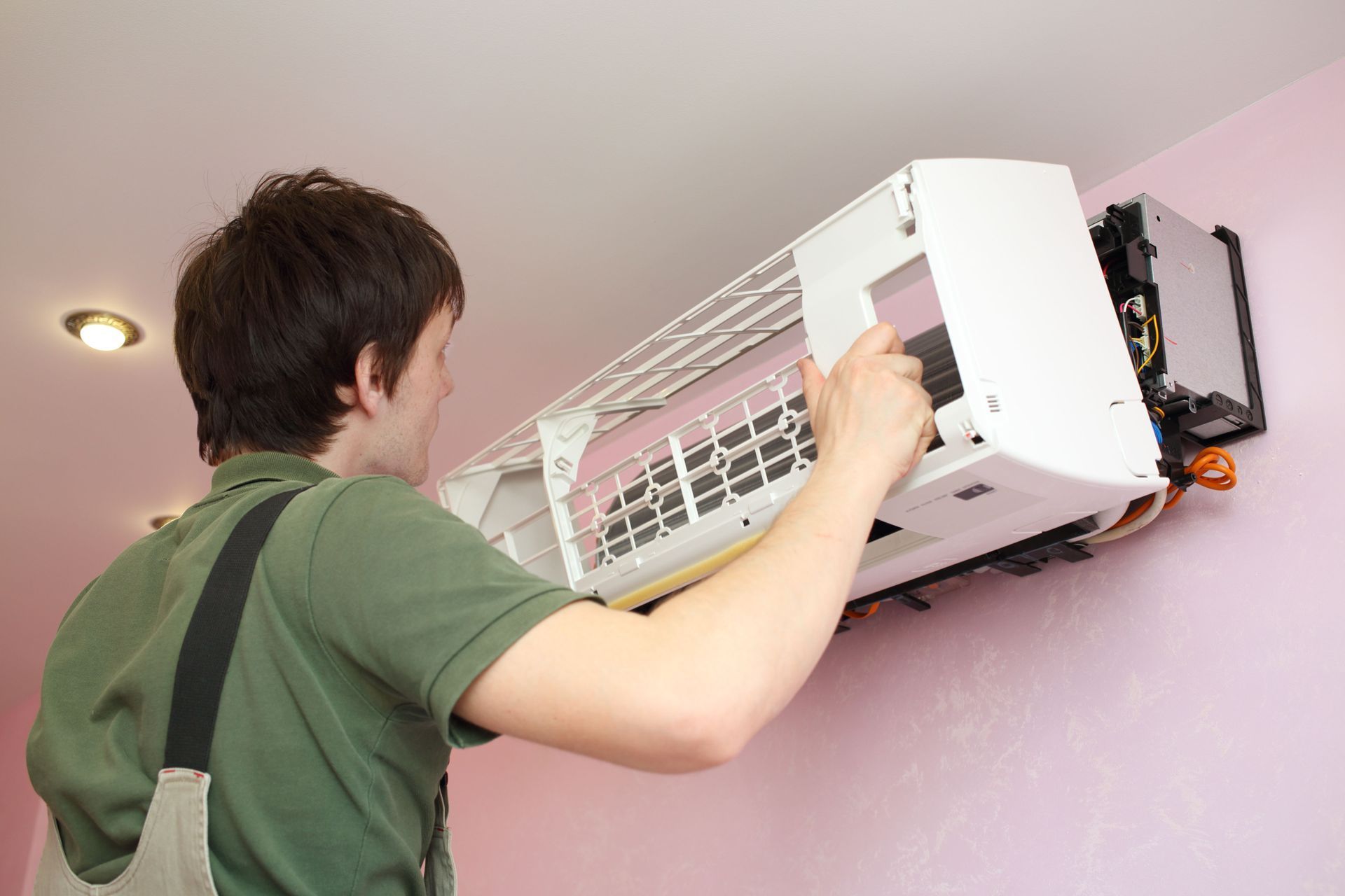 Person installing a white wall-mounted air conditioner in a pink room