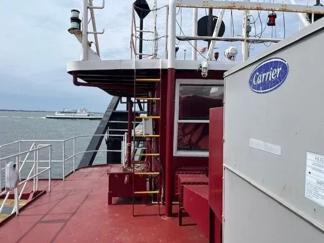 Red ship deck with railings, ladder, and red benches beside open water.