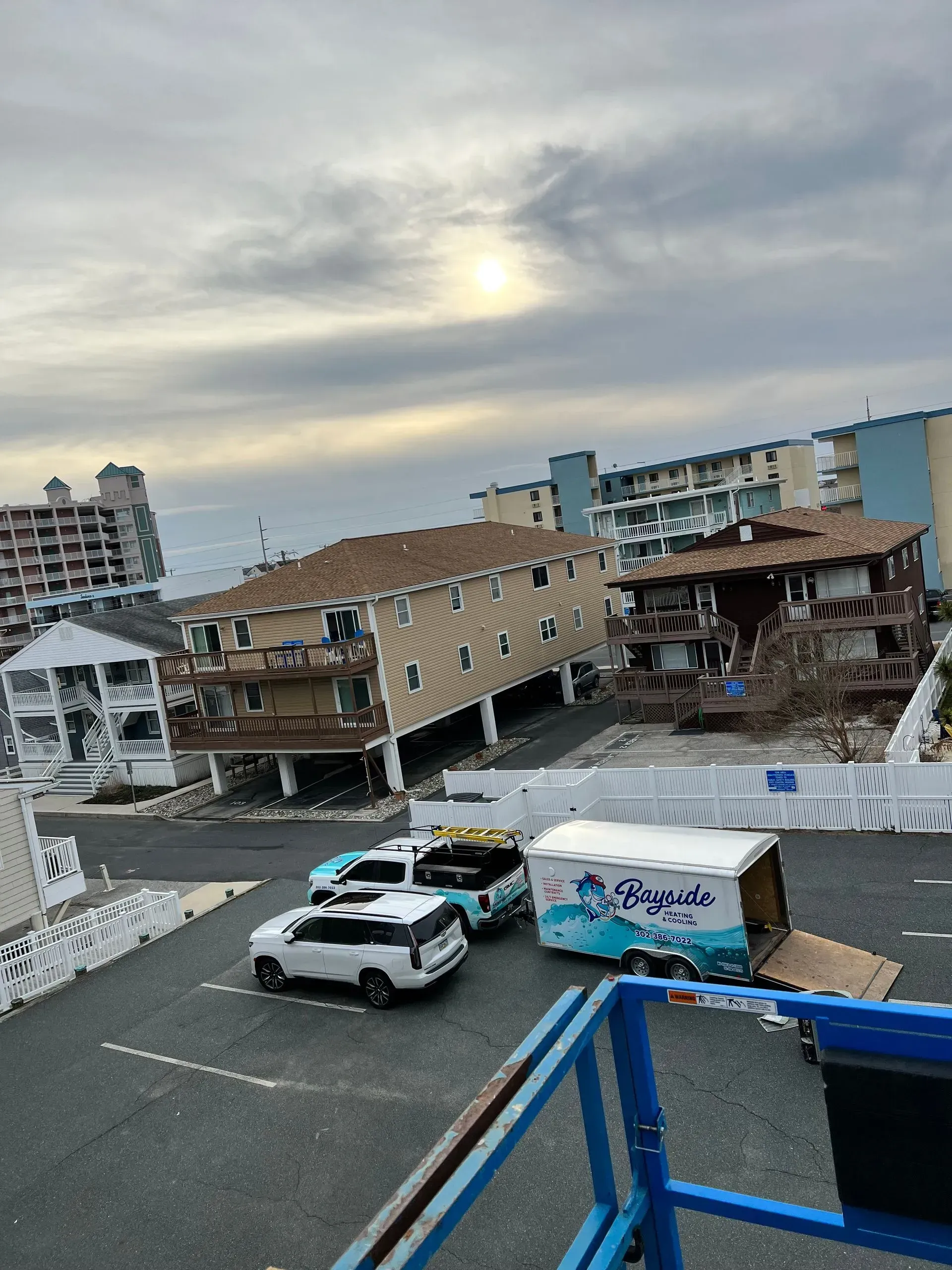 Damaged beachfront buildings and parked cars under a cloudy sky, viewed from a balcony with blue railing