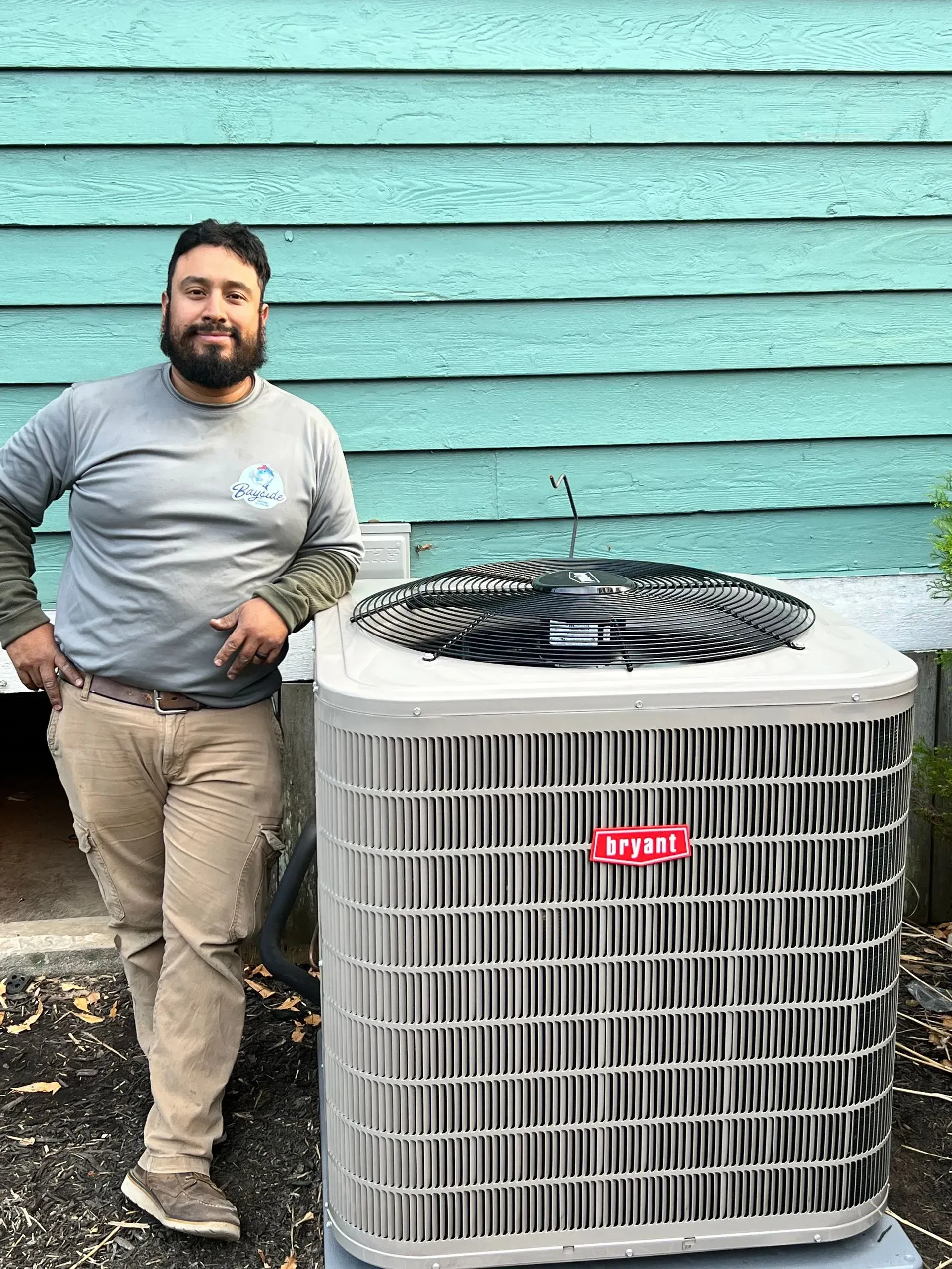Man standing beside a gray outdoor air conditioner unit against a turquoise wall
