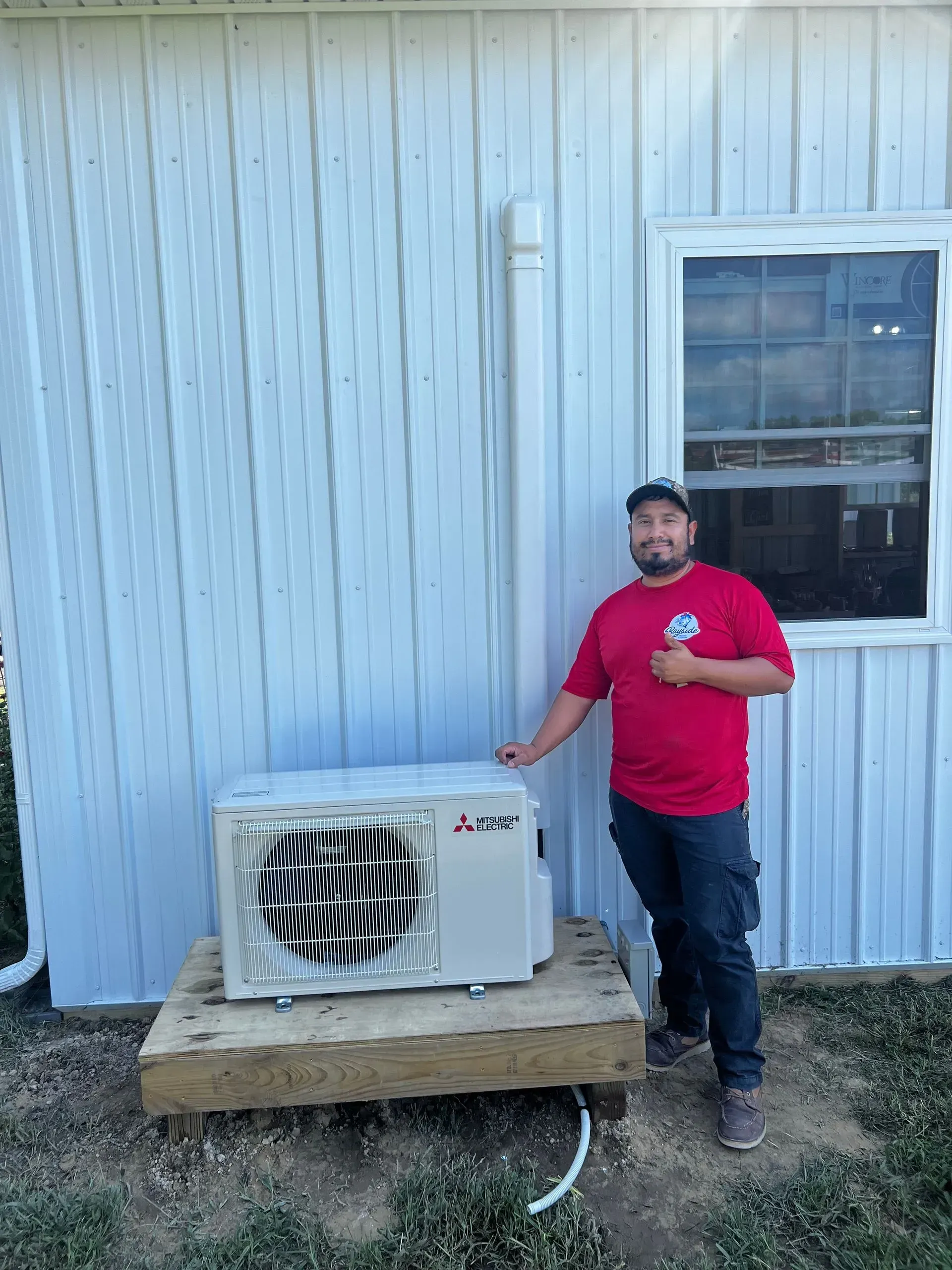 Man standing beside a white outdoor AC unit against a light blue house wall