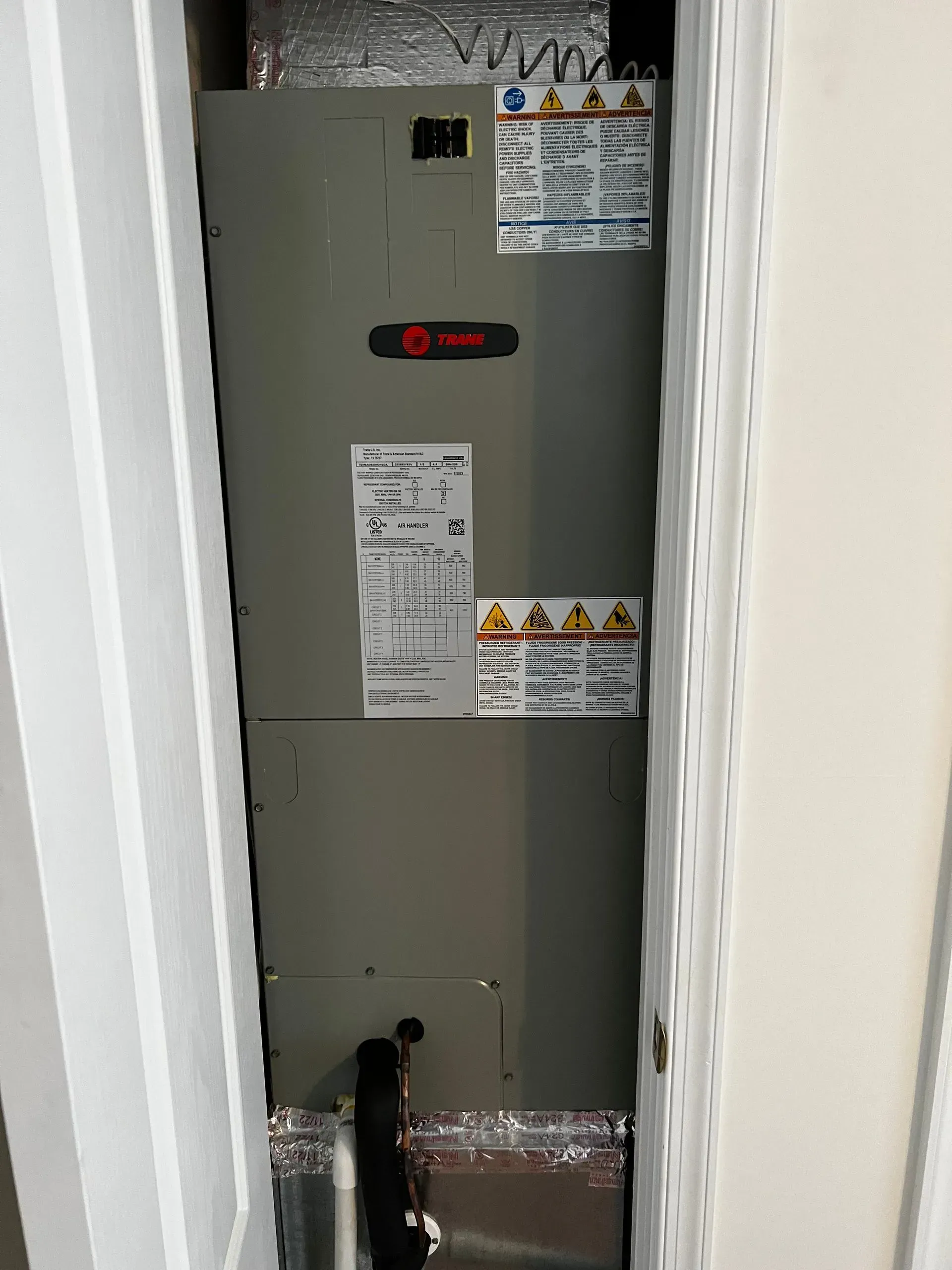 Open electrical panel in a narrow white hallway with warning labels.