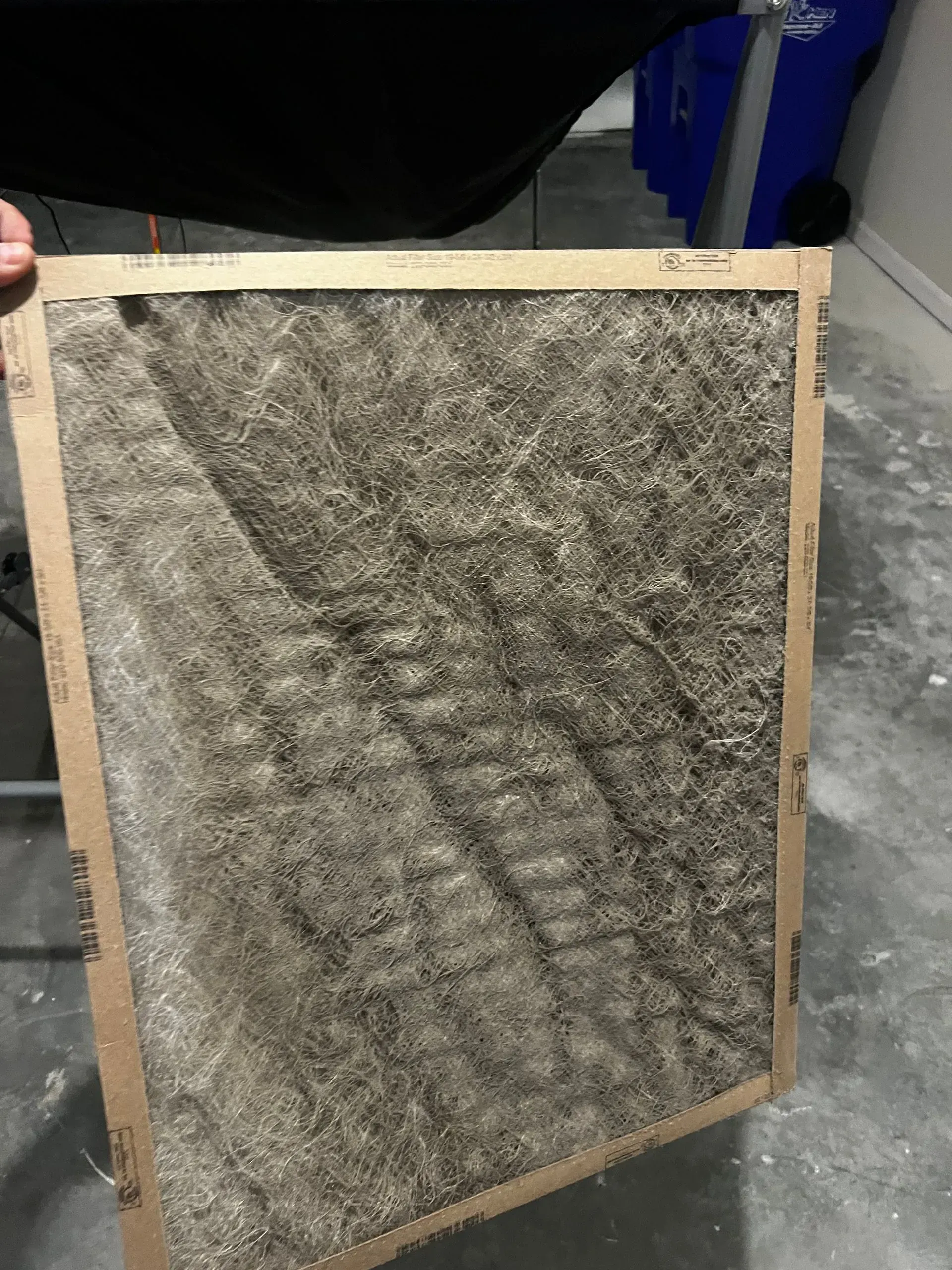 A framed square panel of gray speckled material leaning against a wall on a concrete floor.