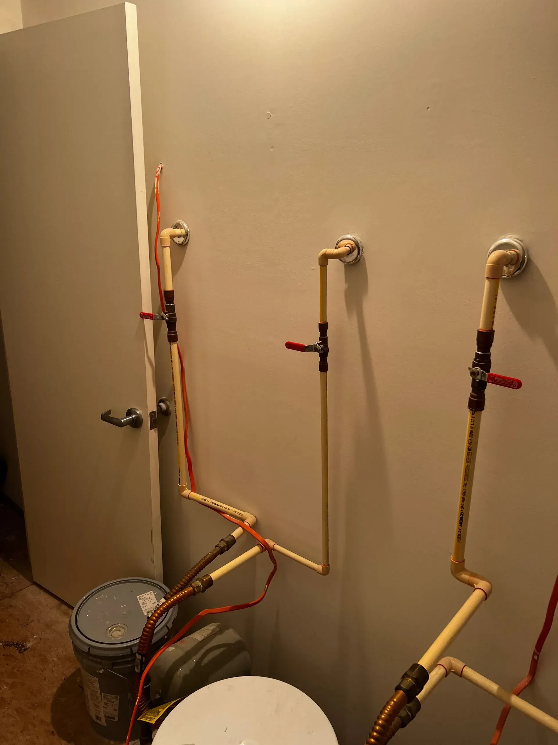 Plumbing pipes and shutoff valves on a wall with exposed copper lines and buckets below