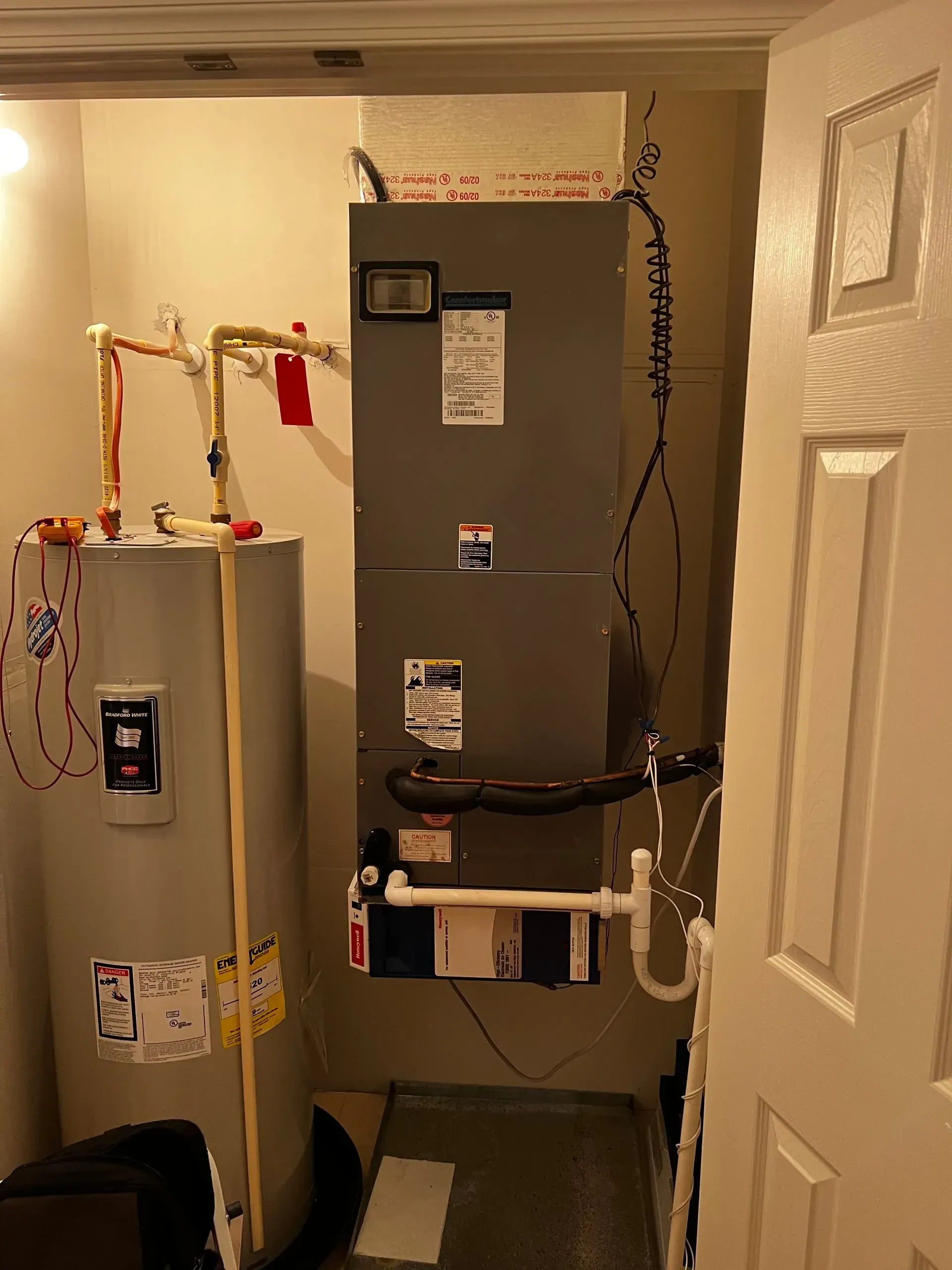 Water heater and furnace in a small utility closet with open door.