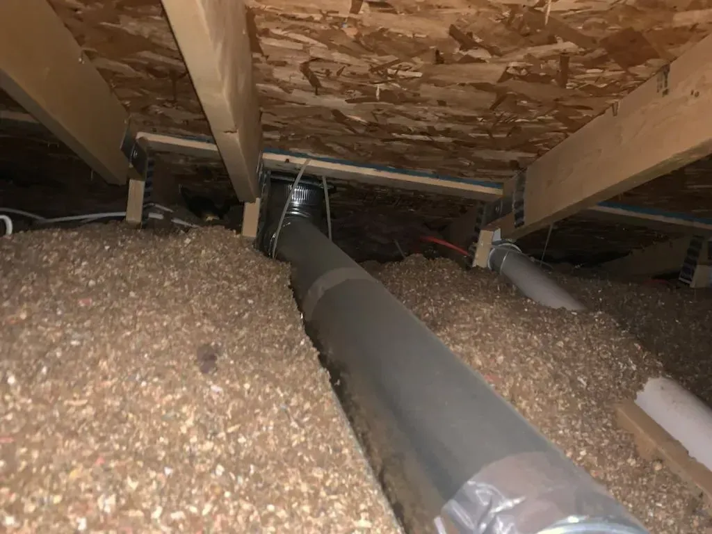 Insulated attic crawlspace with loose fill insulation and a large silver HVAC duct